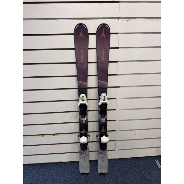 Atomic Maven vus du dessus : skis violets avec logo Atomic doré, fixations blanches et talon gris, devant un mur