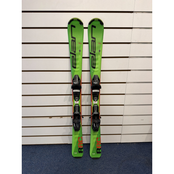 Paire complète de skis enfant Elan RC Race verts avec lettrage Elan noir et fixations, devant un mur à lamelles blanc