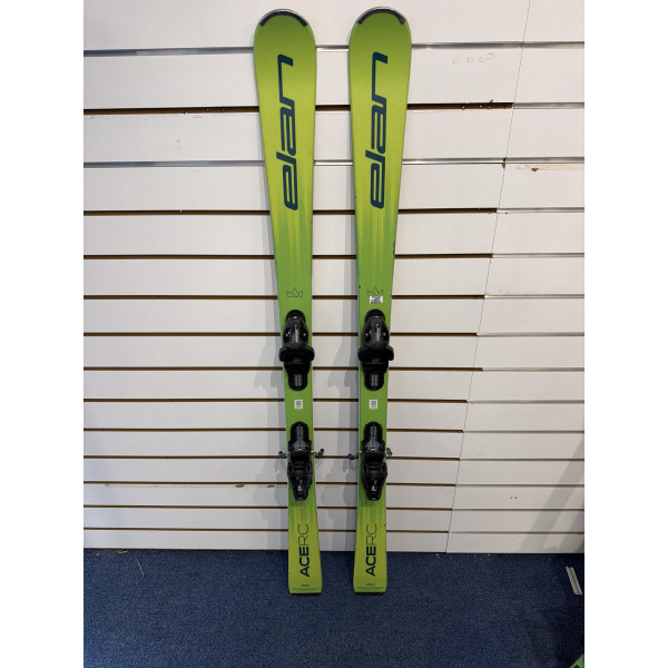 Paire complète de skis junior Elan ACE RC vert citron avec lettrage Elan bleu foncé, devant un mur à lamelles blanc