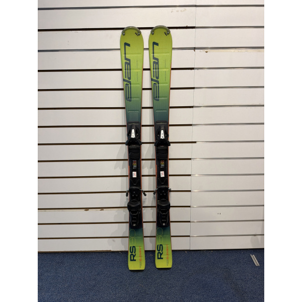Paire complète de skis junior Elan RS Element 80 en dégradé jaune-vert avec fixations, devant un mur à lamelles